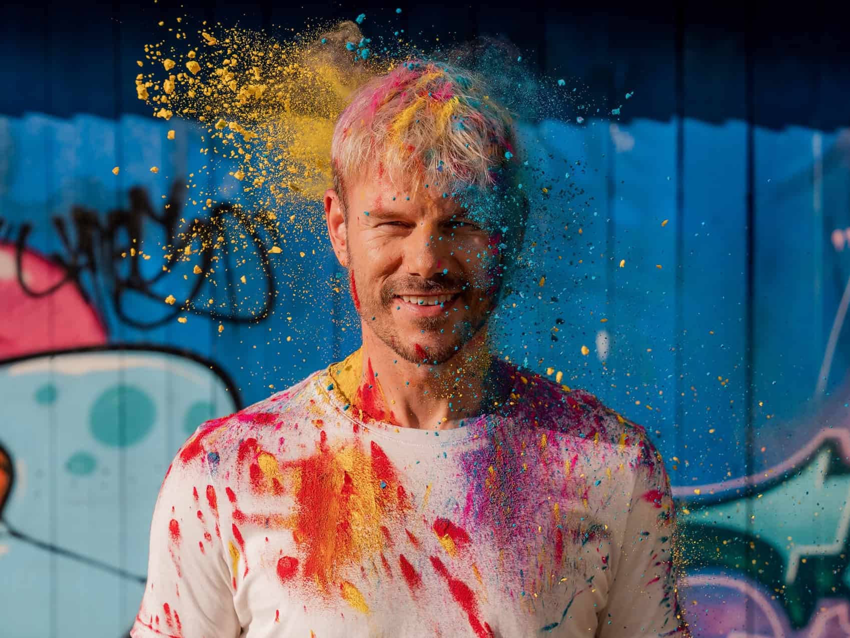 A photograph of Tom Hugo being pelted with brightly coloured poweder